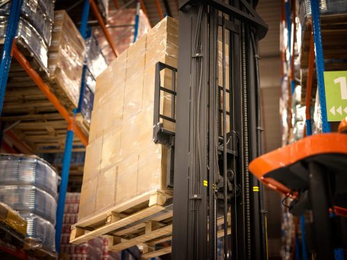 industrial-forklift-machine-lifting-palette-full-cardboard-boxes-placing-them-shelves-distribution-warehouse-facility